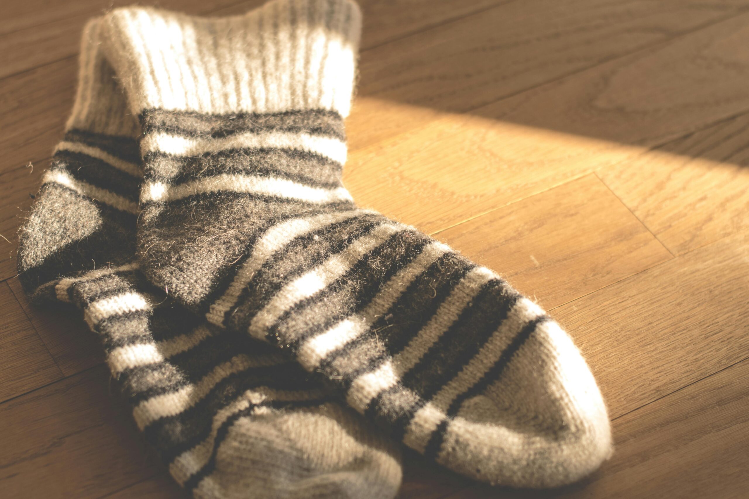 Warm knitted striped socks on a sunlit wooden floor, offering a cozy and stylish winter vibe.